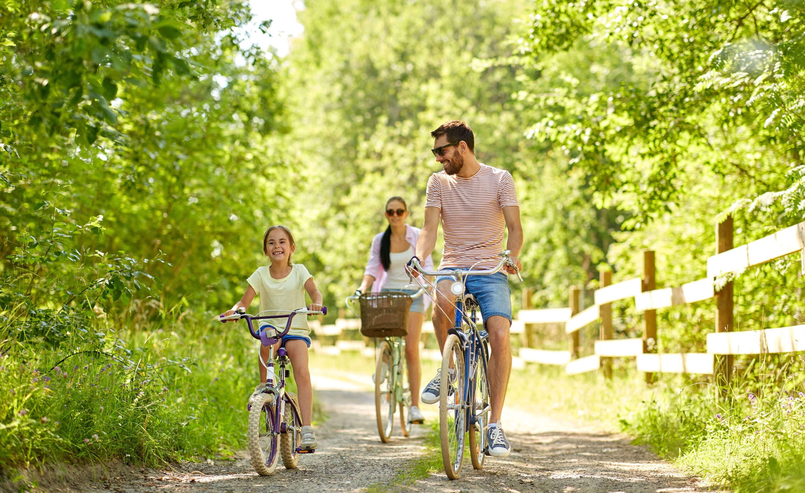 family, leisure and people concept - happy mother, father and little daughter riding bicycles in summer park
