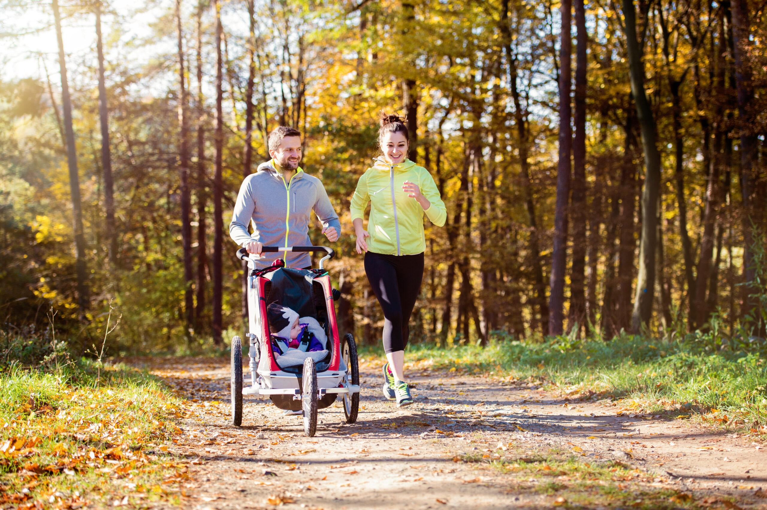 Beautiful young family with baby in jogging stroller running outside in autumn nature